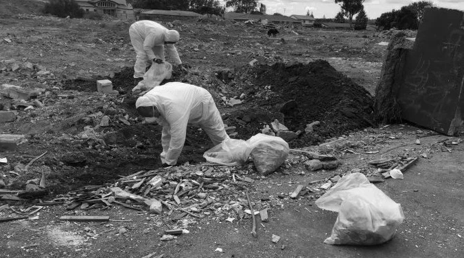 Workers in protective suits removing asbestos-contaminated soil